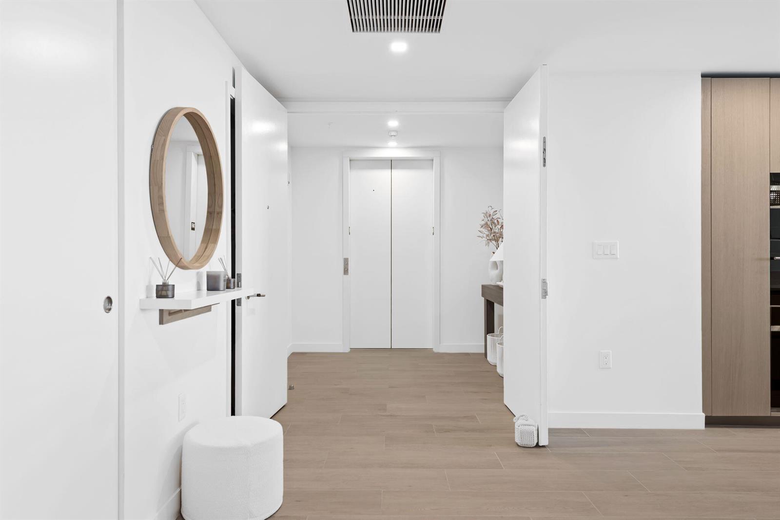 A bright, minimalist entryway features light wood flooring, a round mirror, and a white stool — 900 N Ocean Boulevard # 1404, Pompano Beach FL 33062, POMPANO BEACH, FL