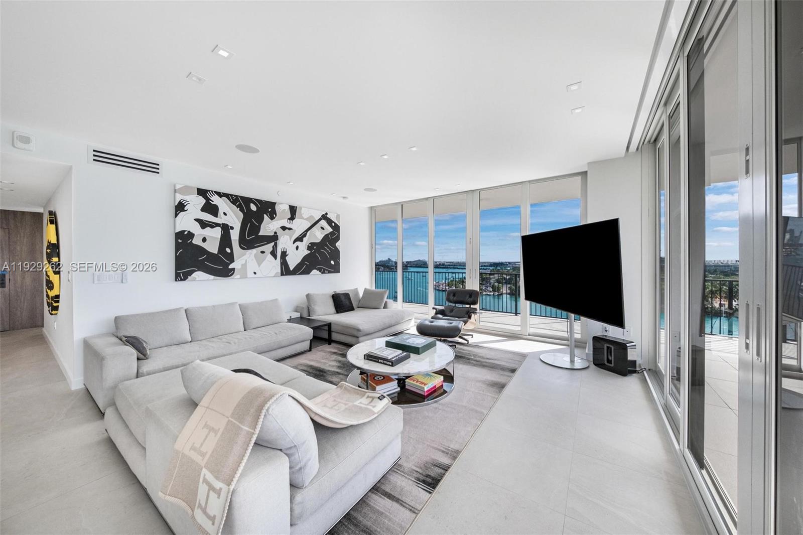 A modern living room features light gray sofas, a round coffee table, and floor-to-ceiling windows — 1000 Venetian Way # 1004, Miami FL 33139, MIAMI, FL