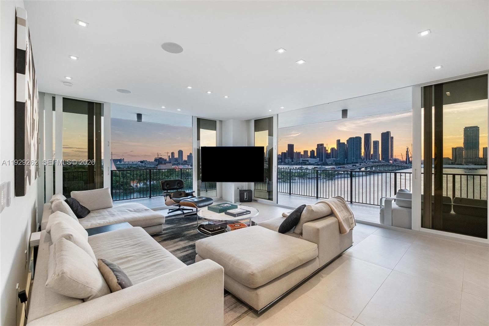 A modern living room features two beige sectionals, a lounge chair, and floor-to-ceiling city views — 1000 Venetian Way # 1004, Miami FL 33139, MIAMI, FL