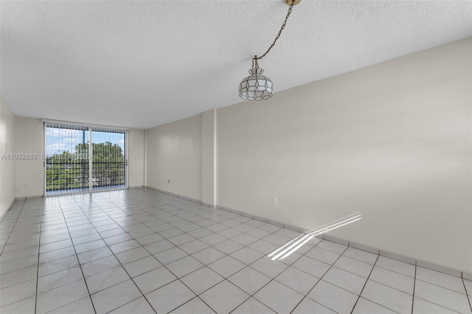 An empty room with white walls, tiled floors, a hanging light fixture, and sliding glass doors — 14180 SW 84th St # G, Miami FL 33183, MIAMI, FL