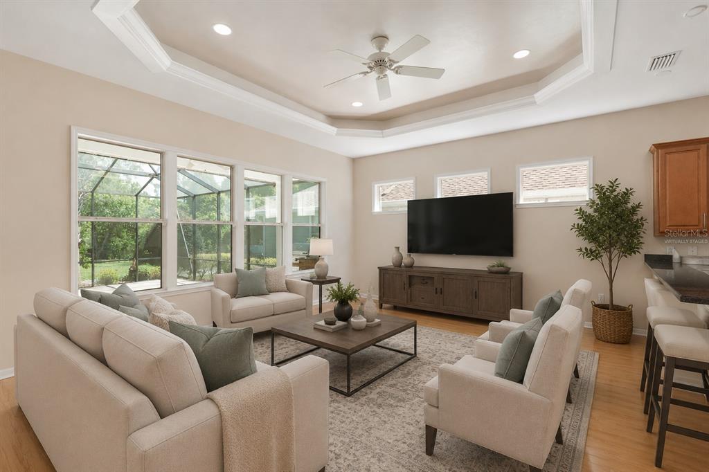 A living room with a tray ceiling, large windows, and neutral furniture on a patterned rug — 8632 SW 76TH PLACE, GAINESVILLE, FL