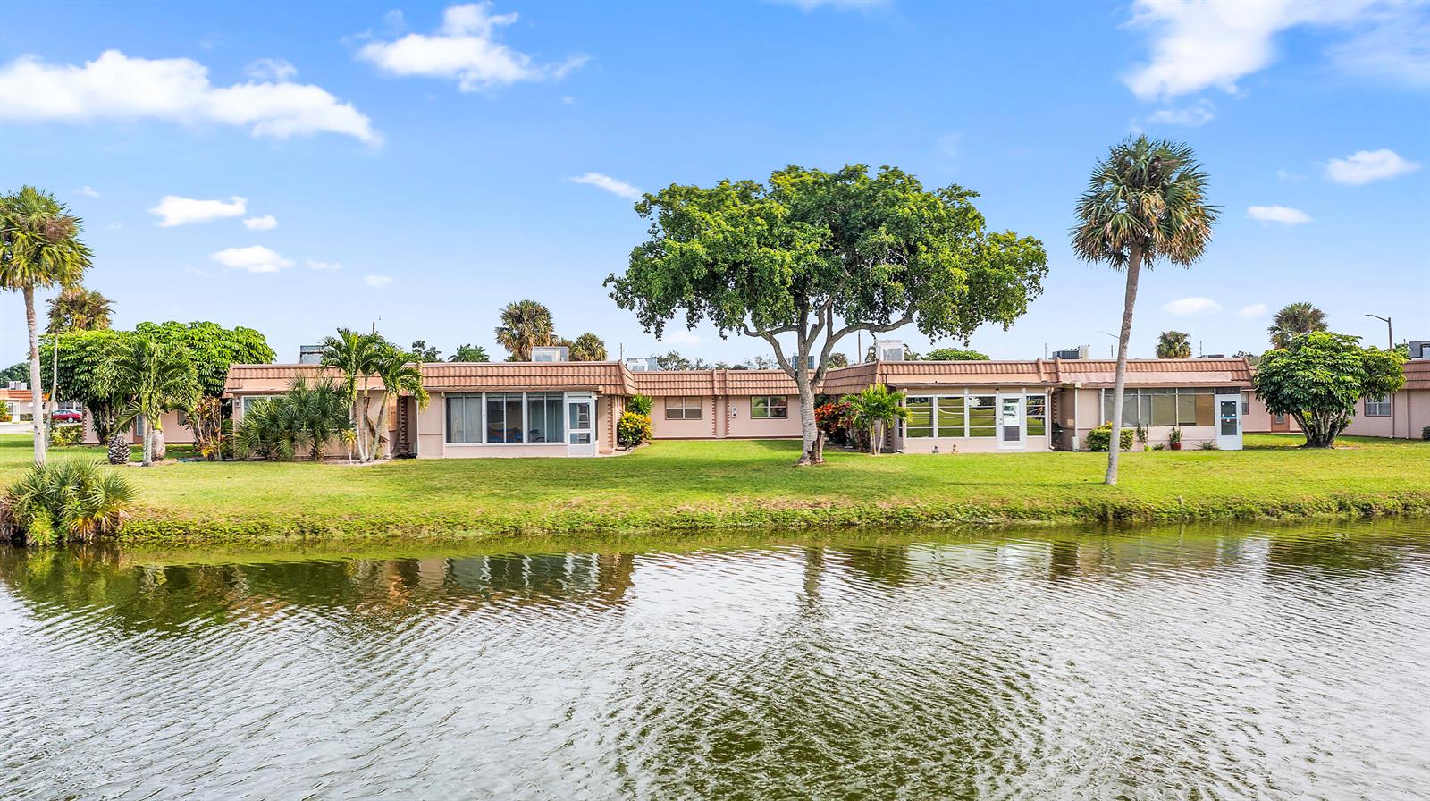 A single-story residential building sits beside a pond with palm trees and green landscaping — 341 Seville O, Delray Beach FL 33446, DELRAY BEACH, FL