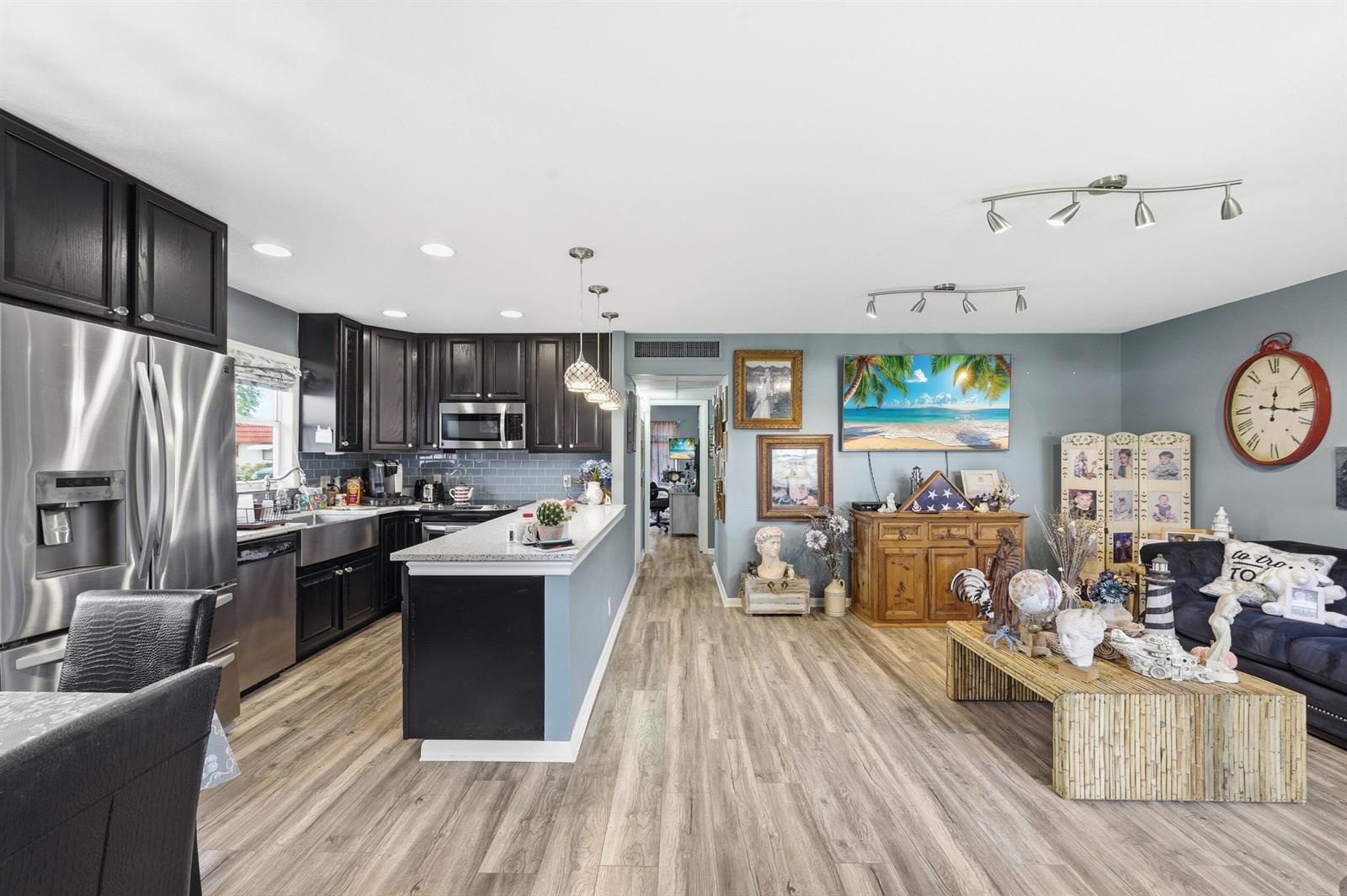 An open-concept kitchen and living area featuring dark cabinetry, stainless steel appliances, and wood-look flooring — 341 Seville O, Delray Beach FL 33446, DELRAY BEACH, FL