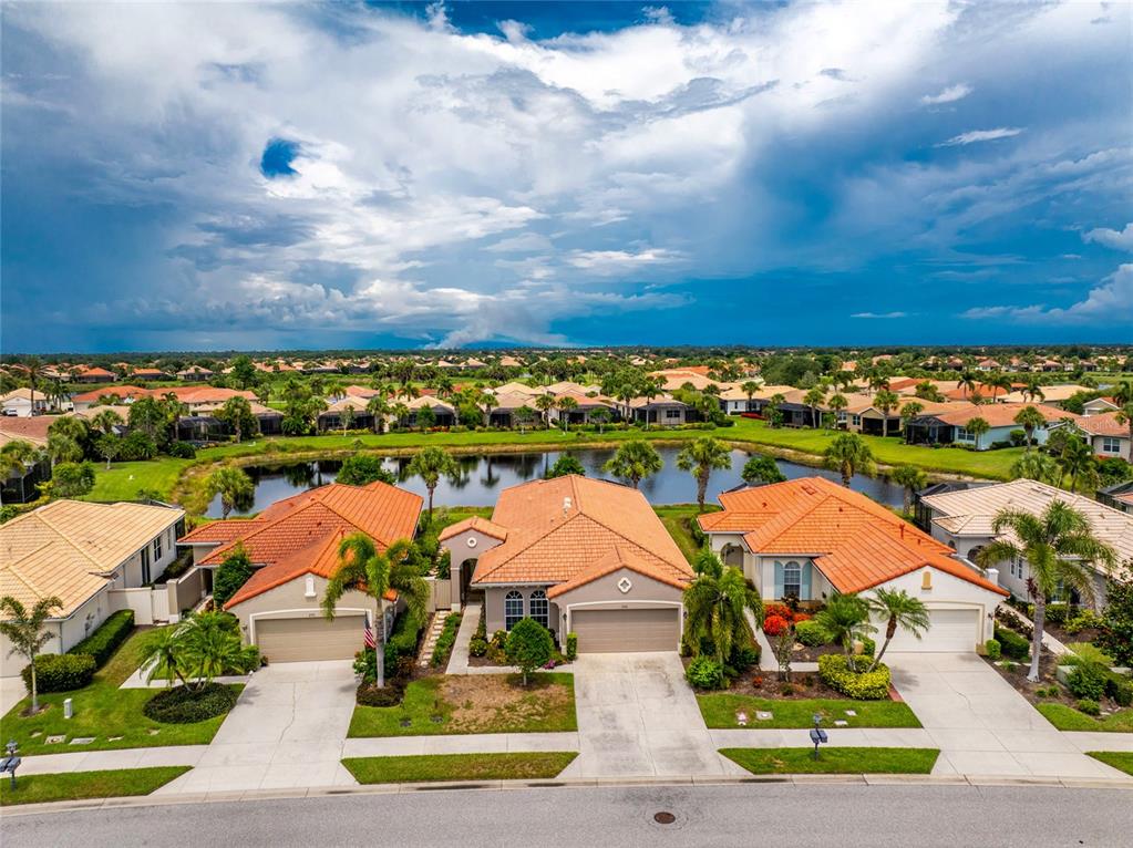 An aerial view shows three suburban houses with orange tile roofs facing a small lake — 246 MESTRE PLACE, NORTH VENICE, FL