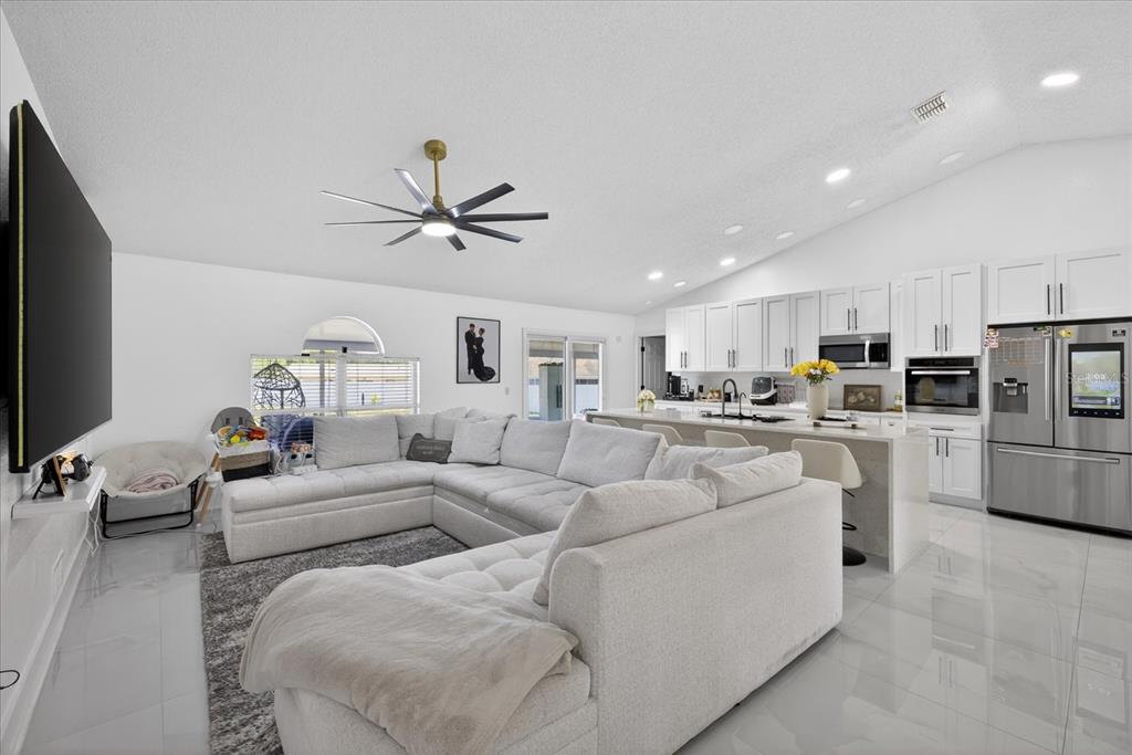 A bright, open-concept living room and kitchen featuring white cabinetry, a large sectional, and tile flooring — 4096 LANDOVER BOULEVARD, SPRING HILL, FL