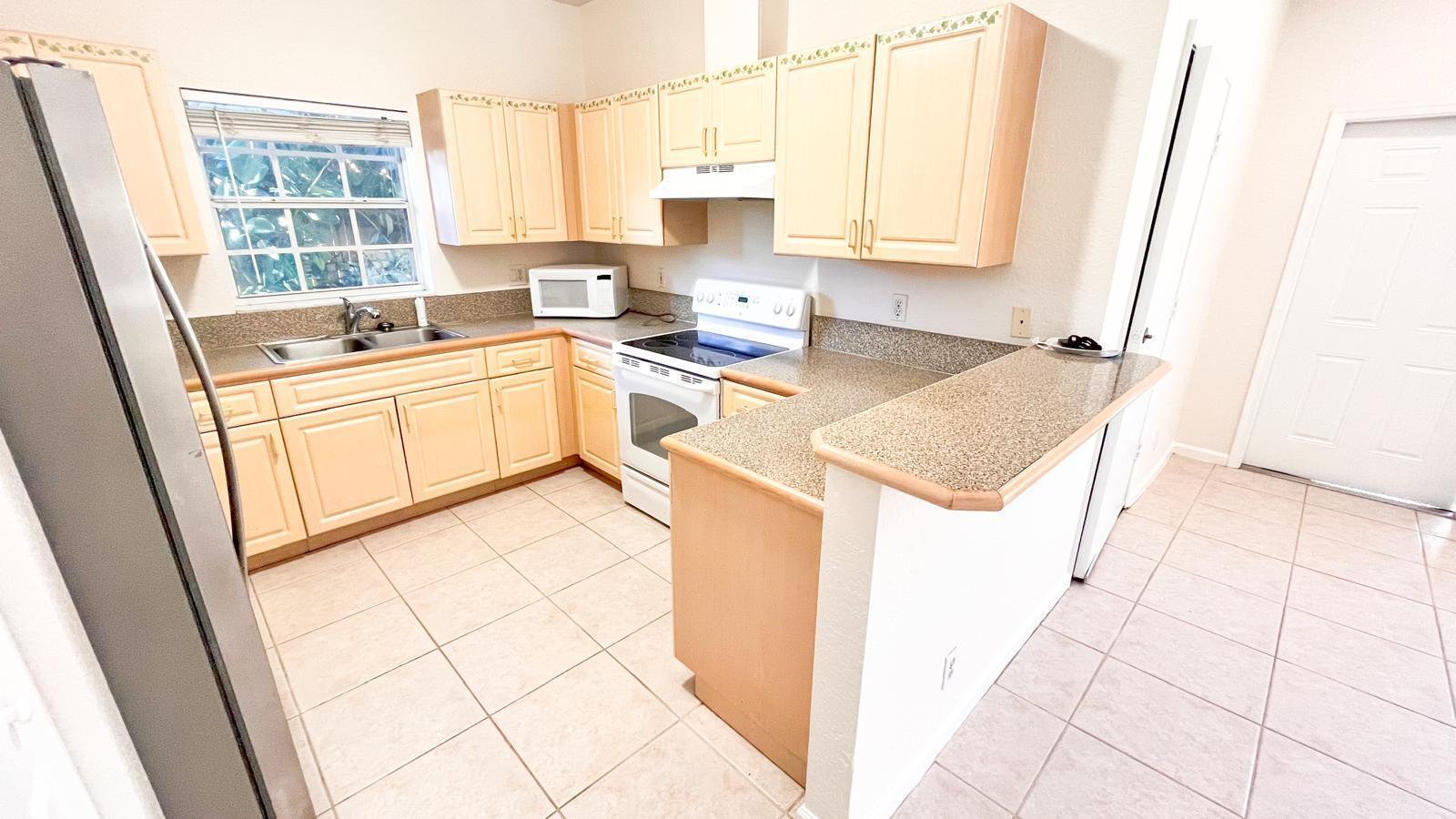 A kitchen features light wood cabinets, speckled laminate countertops, tile flooring, and stainless steel appliances — 1440 Hawthorne Place, Wellington FL 33414, WELLINGTON, FL