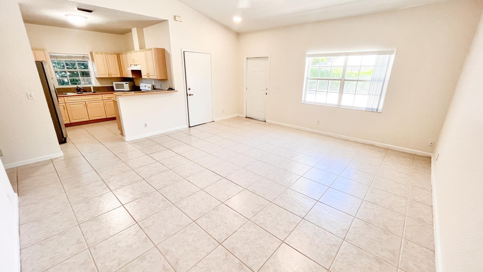 An open-concept living area with light tile flooring, a kitchen, and two white doors — 1440 Hawthorne Place, Wellington FL 33414, WELLINGTON, FL