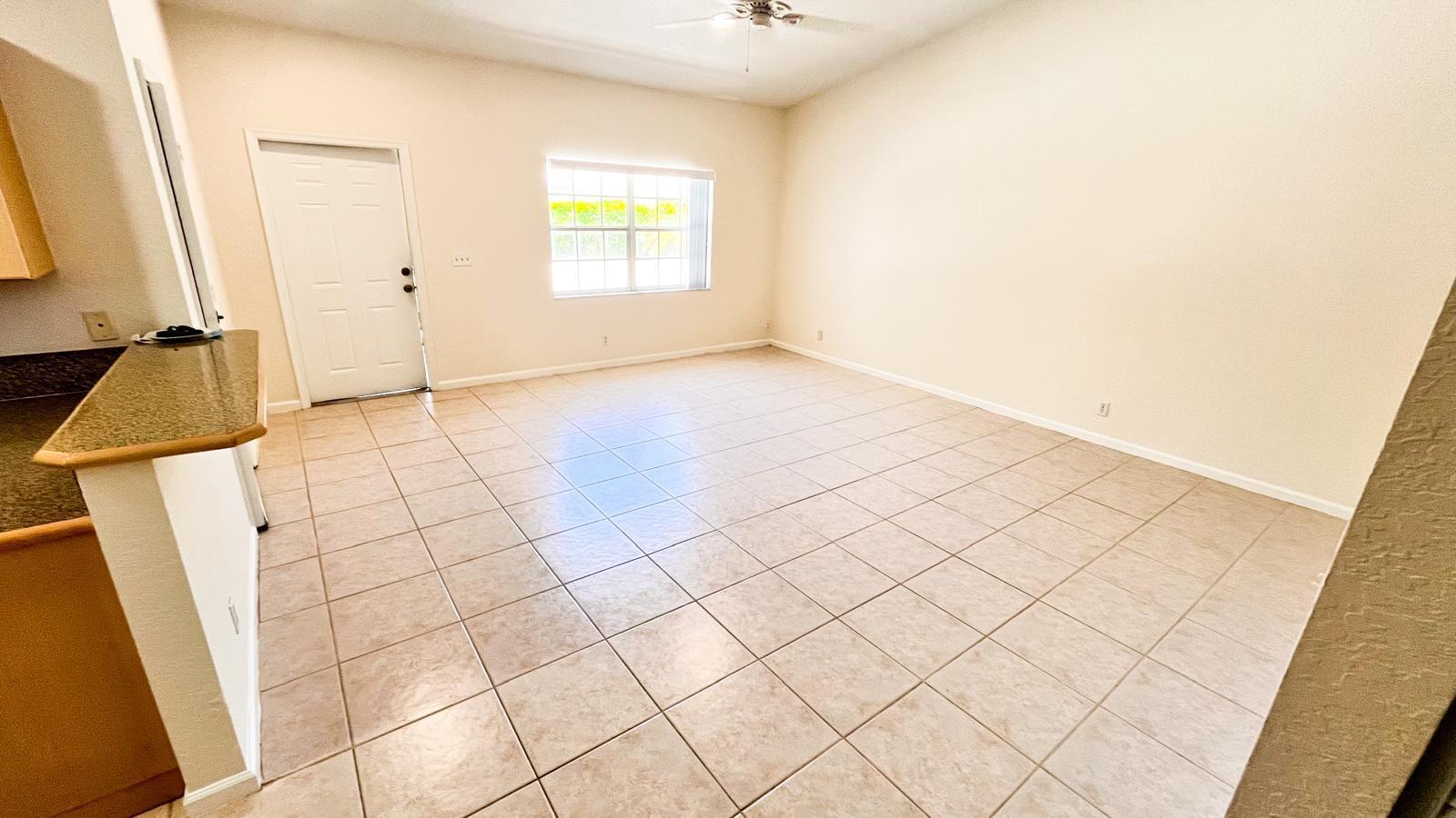An empty room features beige tiled flooring, light-colored walls, a window, and a white door — 1440 Hawthorne Place, Wellington FL 33414, WELLINGTON, FL
