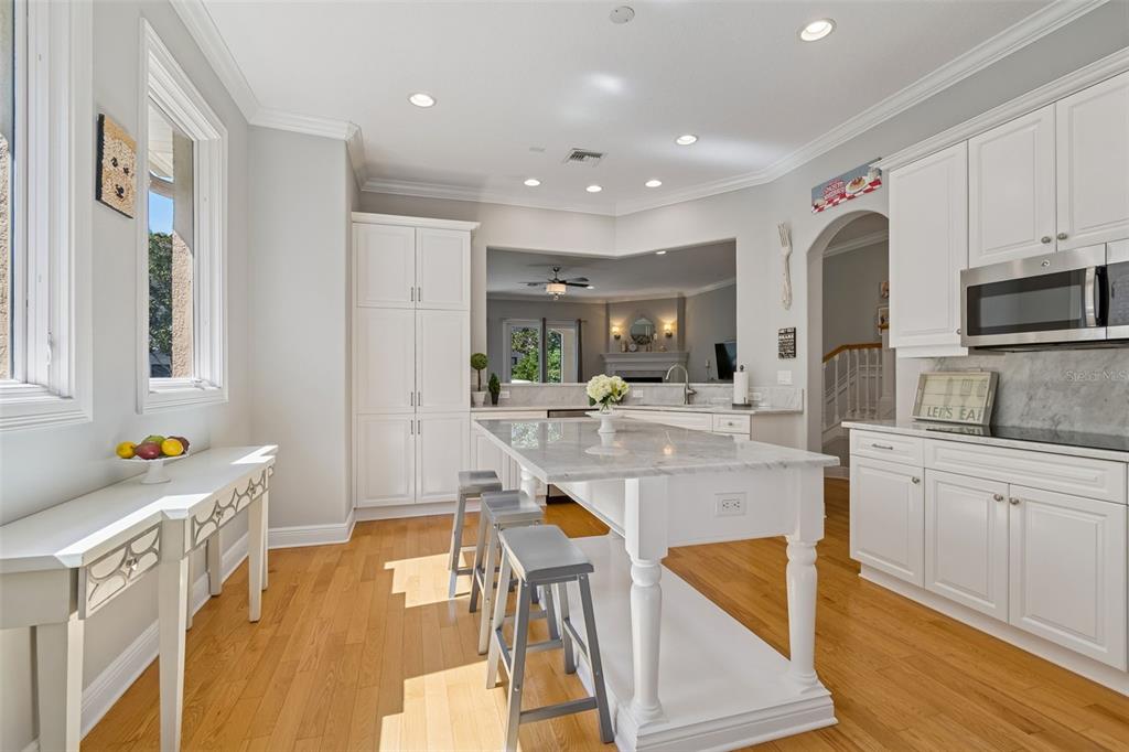A bright kitchen features white cabinetry, a marble-topped island with stools, and hardwood floors — 610 SAXONY BOULEVARD, ST PETERSBURG, FL