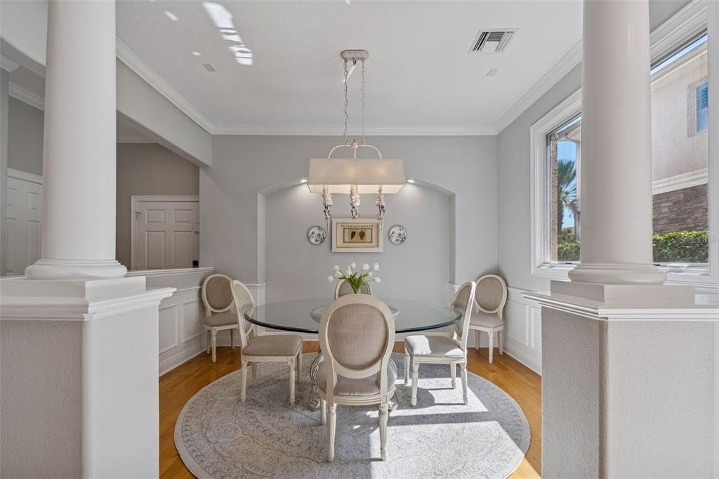 A dining room features a glass-topped table, upholstered chairs, and a chandelier between two columns — 610 SAXONY BOULEVARD, ST PETERSBURG, FL