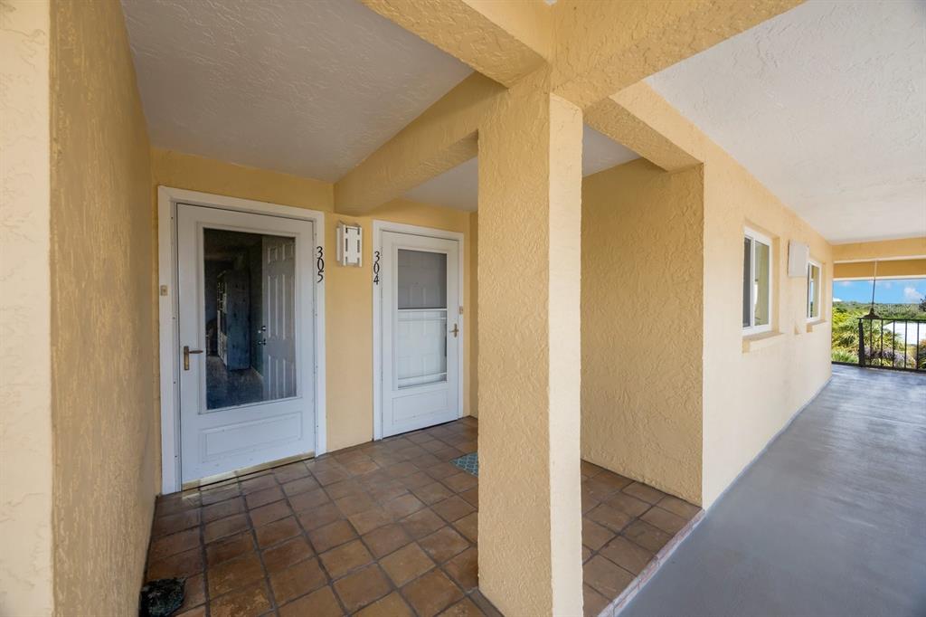 An exterior walkway shows two apartment doors labeled 305 and 304 with tiled flooring — 1125 PINELLAS BAYWAY S UNIT 305, ST PETERSBURG, FL