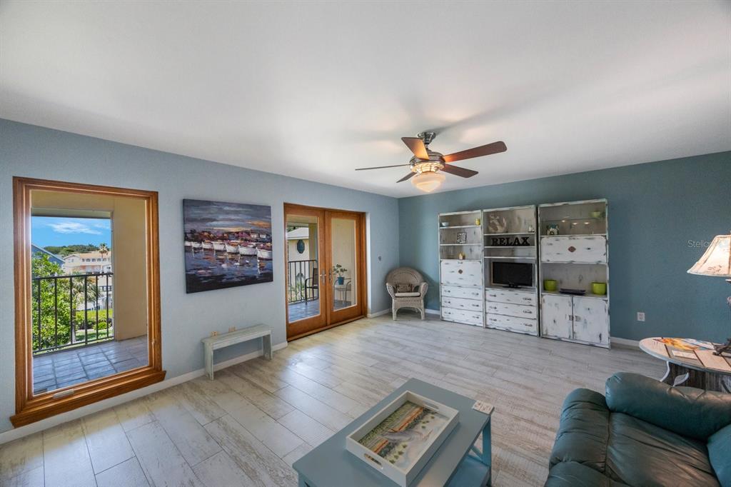 A living room features light blue walls, wood-look tile flooring, a ceiling fan, and balcony access — 1125 PINELLAS BAYWAY S UNIT 305, ST PETERSBURG, FL