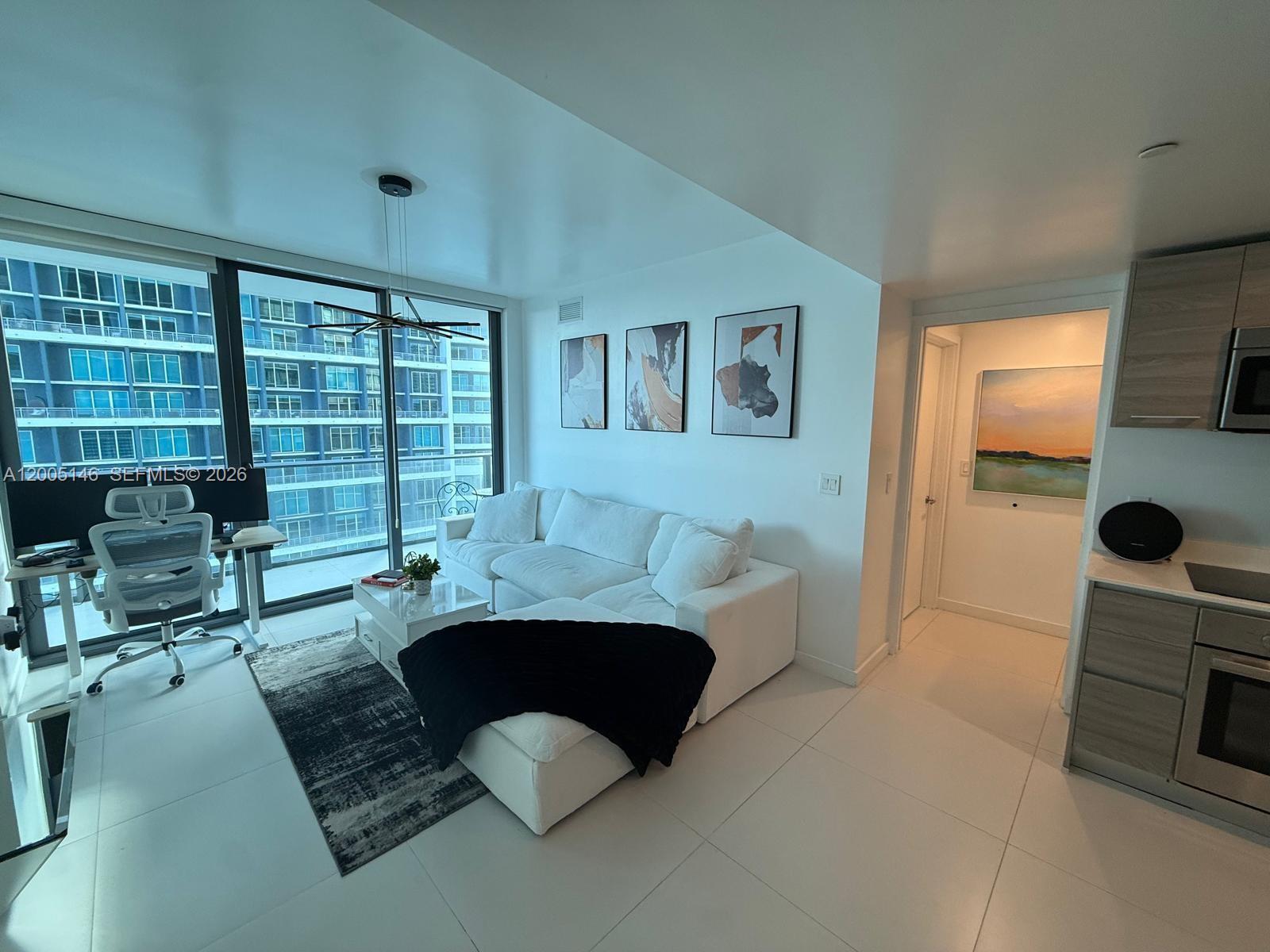 A modern living room features a white sectional sofa, a desk, and floor-to-ceiling windows — 1300 S Miami Ave # 3107, Miami FL 33130, MIAMI, FL