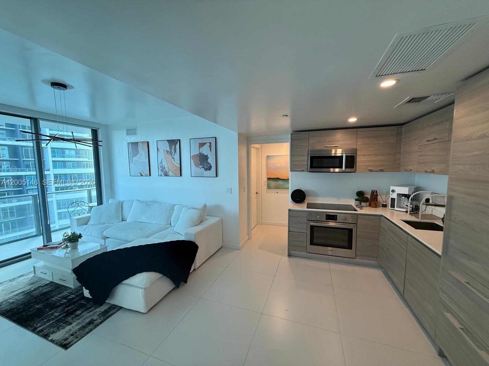 A modern open-concept living room and kitchen with white tile floors and light wood cabinetry — 1300 S Miami Ave # 3107, Miami FL 33130, MIAMI, FL