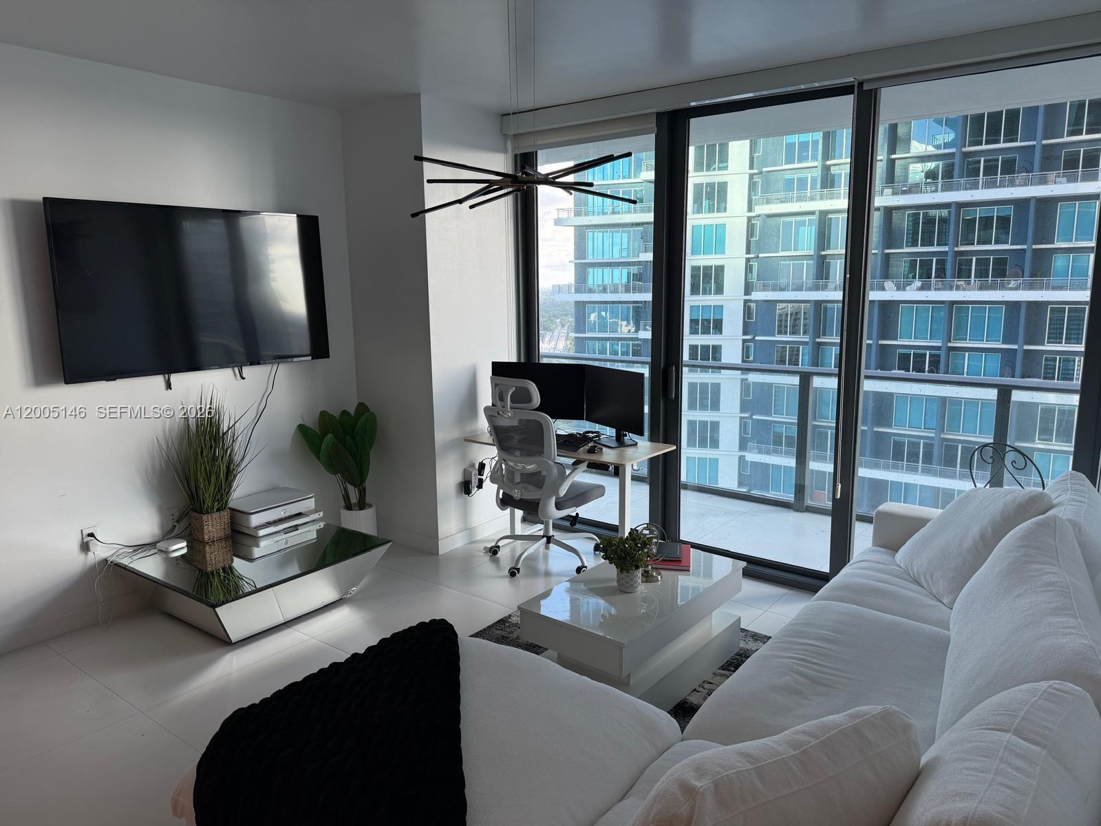 A modern living room features a white sofa, a mirrored media console, and a workspace — 1300 S Miami Ave # 3107, Miami FL 33130, MIAMI, FL
