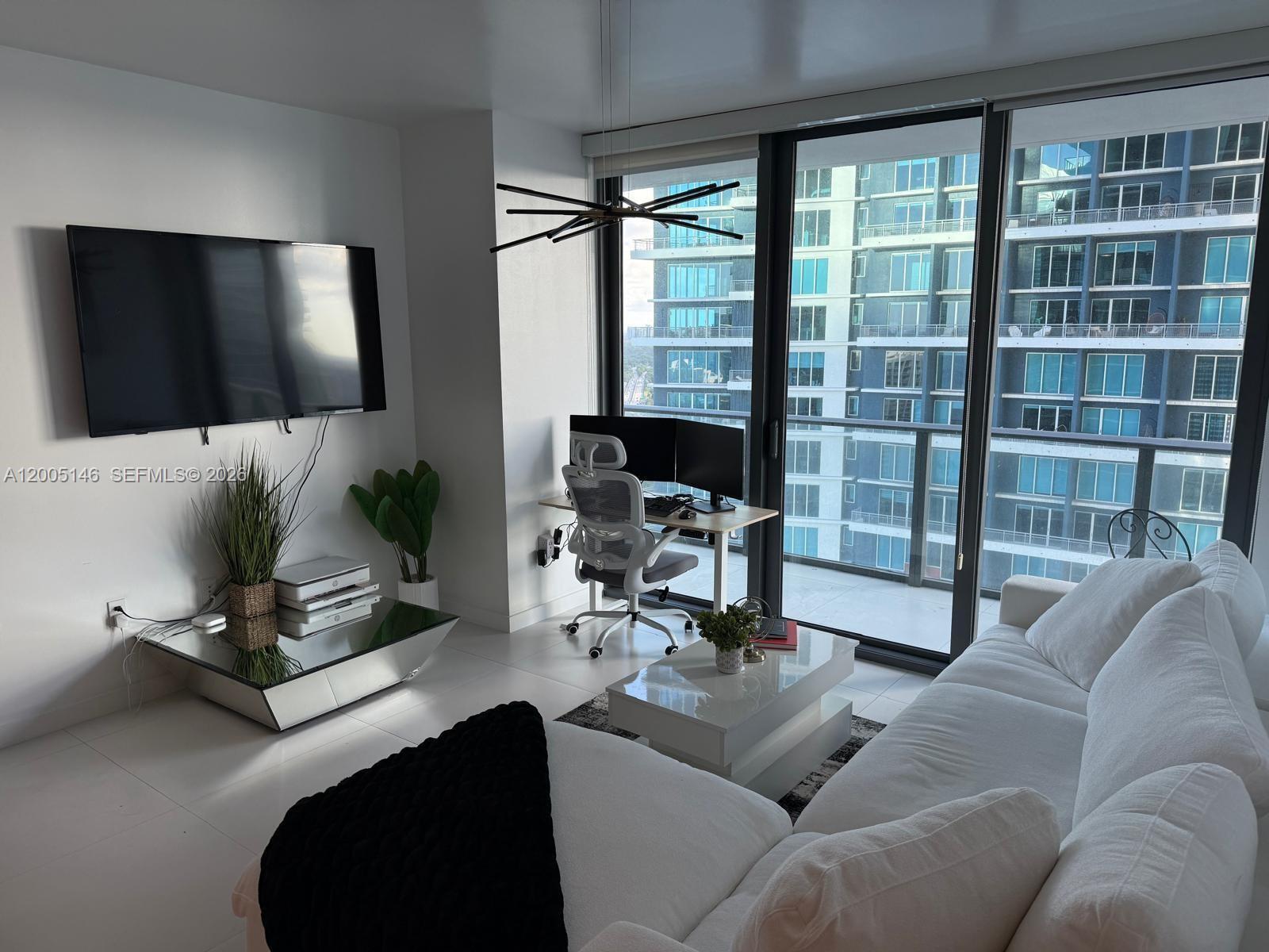 A modern living room features a white sofa, a mirrored coffee table, and a desk area — 1300 S Miami Ave # 3107, Miami FL 33130, MIAMI, FL
