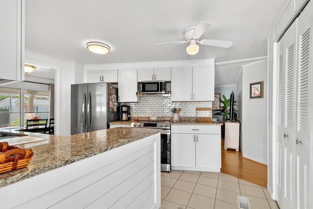 A kitchen features white cabinets, granite countertops, stainless steel appliances, and a tiled backsplash — 42 CABALLO WAY, BRADENTON, FL