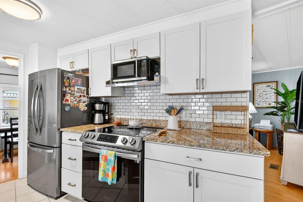 A kitchen features white cabinets, granite countertops, a subway tile backsplash, and stainless steel appliances — 42 CABALLO WAY, BRADENTON, FL