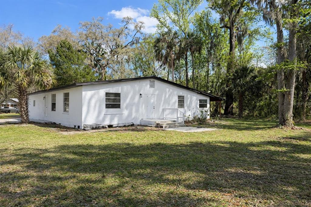 A white, single-story house with a low-pitched roof sits on a grassy, wooded lot — 502 NW CRYSTAL STREET, CRYSTAL RIVER, FL