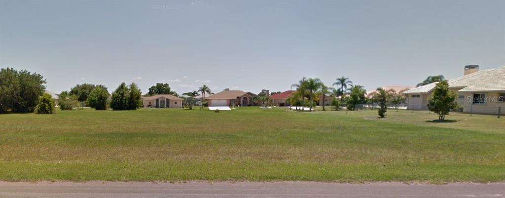A wide, grassy vacant lot is situated in a residential neighborhood with surrounding houses — 11663 SW DALLAS DRIVE N, LAKE SUZY, FL