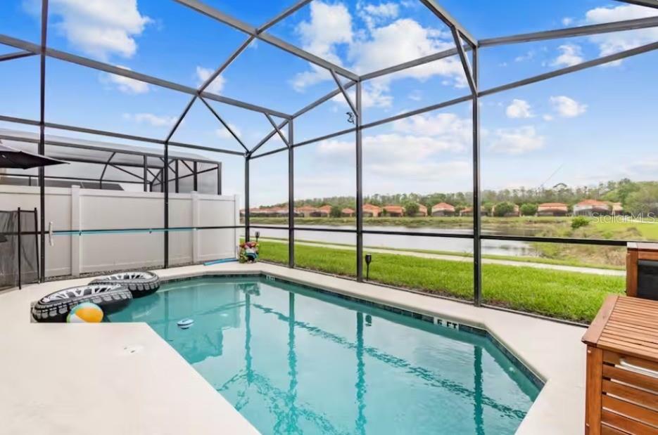 A screened-in swimming pool overlooks a lake and a row of houses in the distance — 471 LAS FUENTES DRIVE, KISSIMMEE, FL