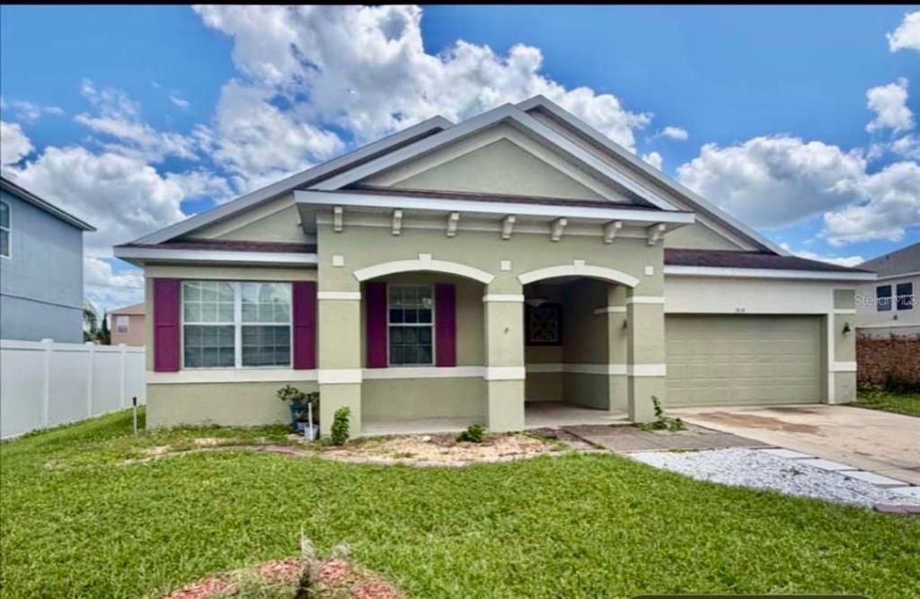 A single-story house with light green stucco siding, a two-car garage, and a covered porch — 3514 PINTAIL LANE, ST CLOUD, FL