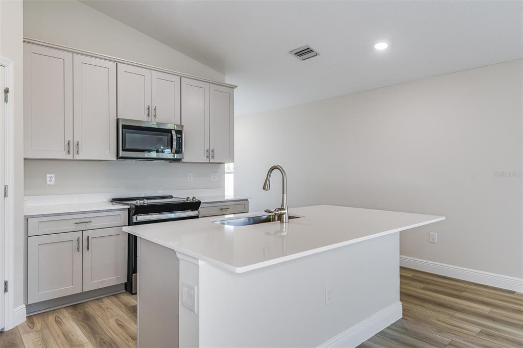 A kitchen features light gray cabinets, white countertops, a central island, and wood-look flooring — 6132 SW 96TH PLACE, OCALA, FL