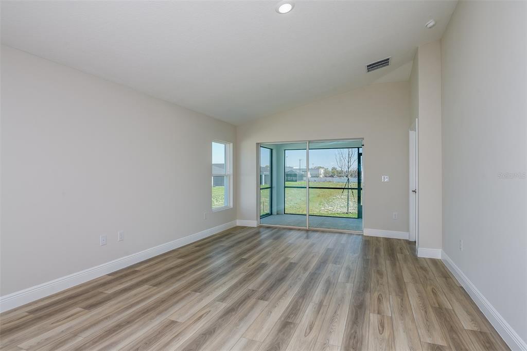An empty room with light wood-look flooring, vaulted ceilings, and a sliding glass door — 6132 SW 96TH PLACE, OCALA, FL