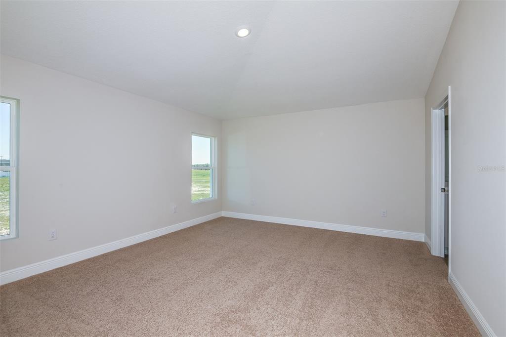An empty bedroom features beige carpet, light walls, two windows, and a doorway — 6132 SW 96TH PLACE, OCALA, FL