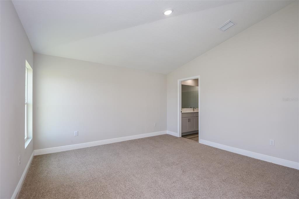 An empty bedroom with beige carpet, light-colored walls, a vaulted ceiling, and an attached bathroom — 6132 SW 96TH PLACE, OCALA, FL