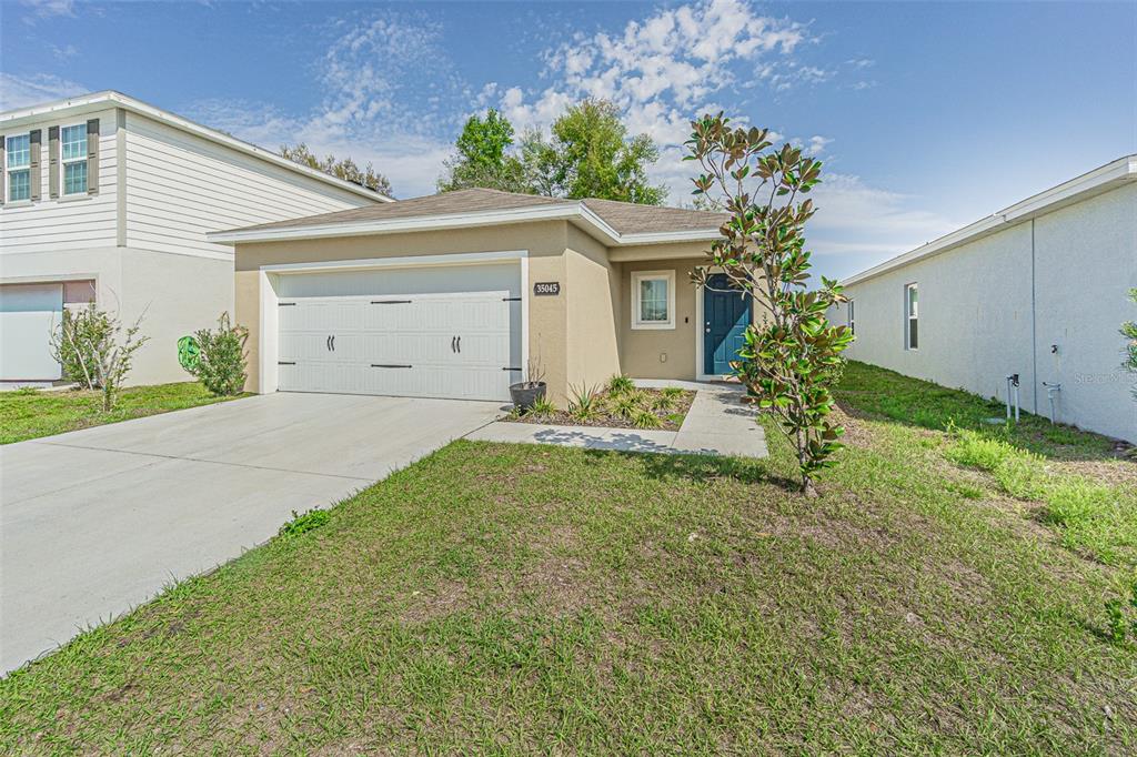 A single-story suburban house with a tan stucco exterior, a two-car garage, and a driveway — 35045 JOMAR AVENUE, ZEPHYRHILLS, FL
