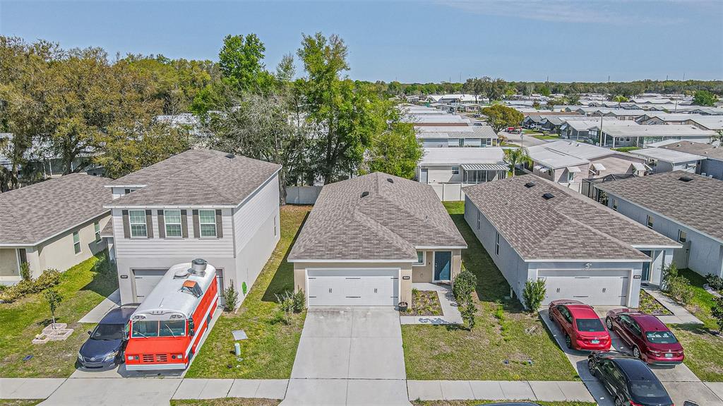 An aerial view shows three suburban houses with driveways, a red bus, and several parked cars — 35045 JOMAR AVENUE, ZEPHYRHILLS, FL