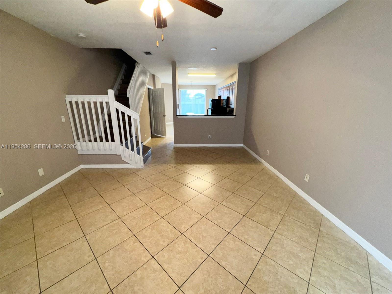 An open living area features tile flooring, a staircase with white railings, and a kitchen pass-through — 3622 Oleander Ter, Riviera Beach FL 33404, RIVIERA BEACH, FL