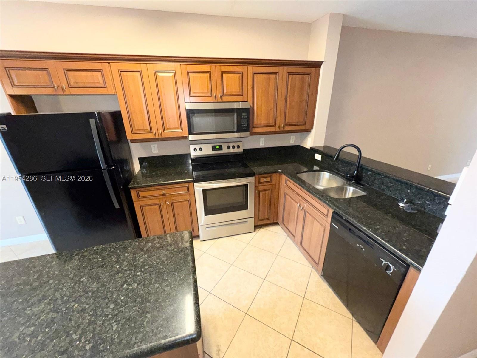 A kitchen features wood cabinets, black appliances, dark granite countertops, and light tile flooring — 3622 Oleander Ter, Riviera Beach FL 33404, RIVIERA BEACH, FL