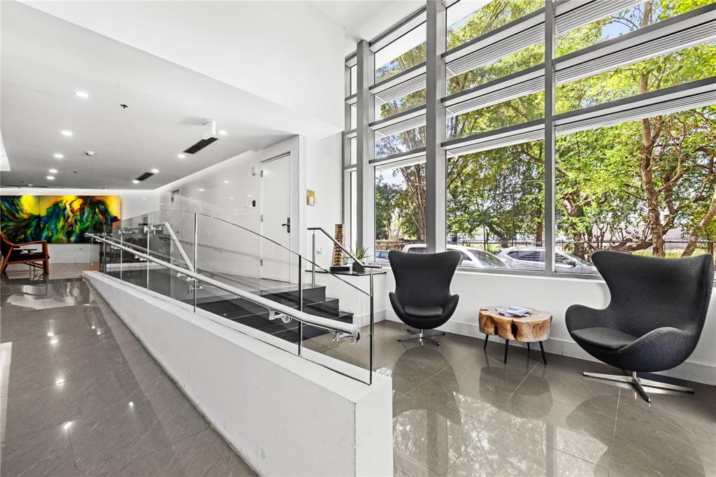 A modern lobby features gray tiled floors, two dark egg chairs, and floor-to-ceiling windows — 1212 LUCHETTI ST UNIT PH, SAN JUAN, PR