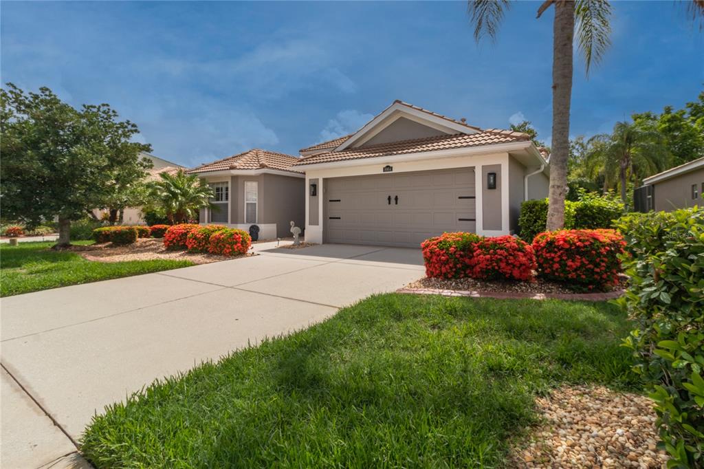 A single-story house with a beige exterior, a two-car garage, and red flowering bushes — 8964 STONE HARBOUR LOOP, BRADENTON, FL
