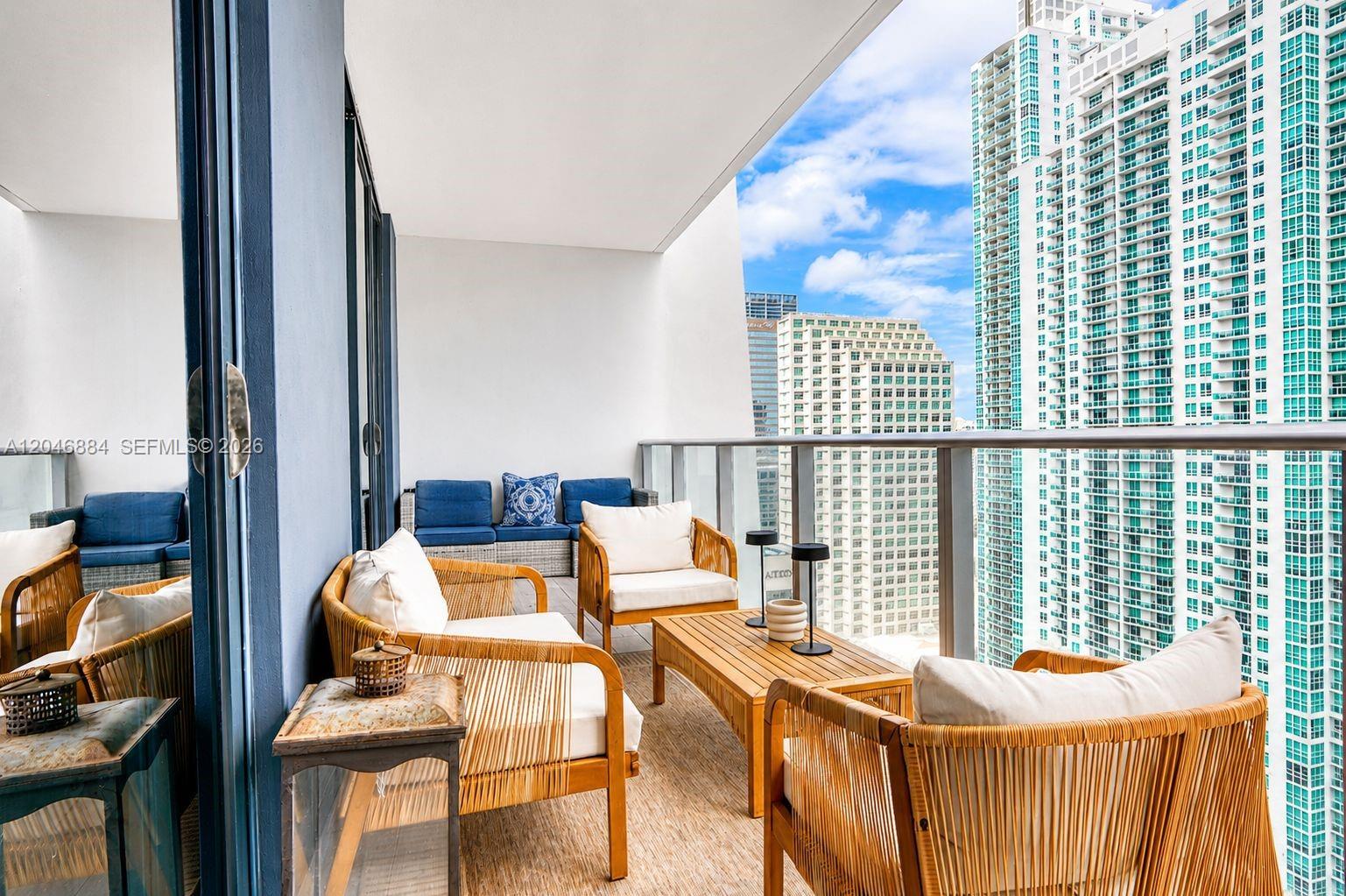 A high-rise balcony features wicker furniture, white cushions, and a view of surrounding skyscrapers — 1010 Brickell Ave # 2402, Miami FL 33131, MIAMI, FL
