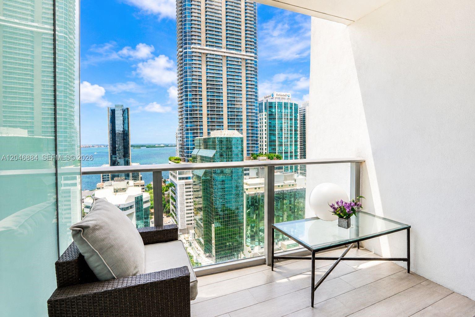 A balcony with wicker furniture overlooks a city skyline and a body of water — 1010 Brickell Ave # 2402, Miami FL 33131, MIAMI, FL