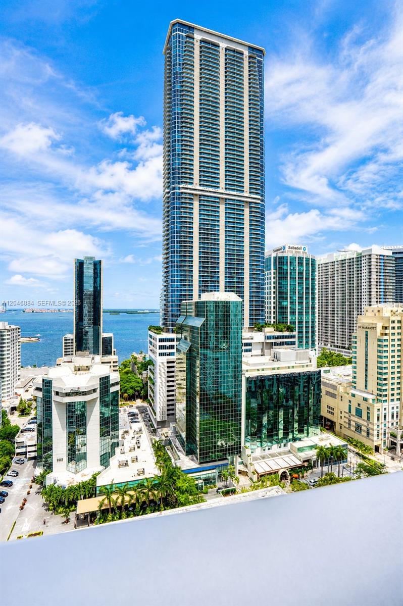 An aerial view shows a tall glass skyscraper surrounded by other buildings and the ocean — 1010 Brickell Ave # 2402, Miami FL 33131, MIAMI, FL