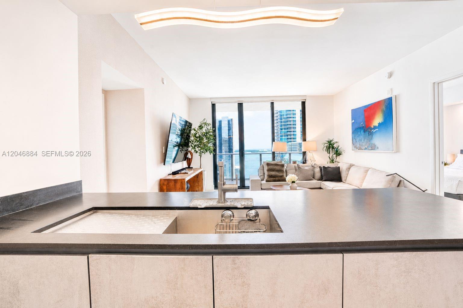 A modern kitchen island with a sink overlooks a living area with floor-to-ceiling windows — 1010 Brickell Ave # 2402, Miami FL 33131, MIAMI, FL