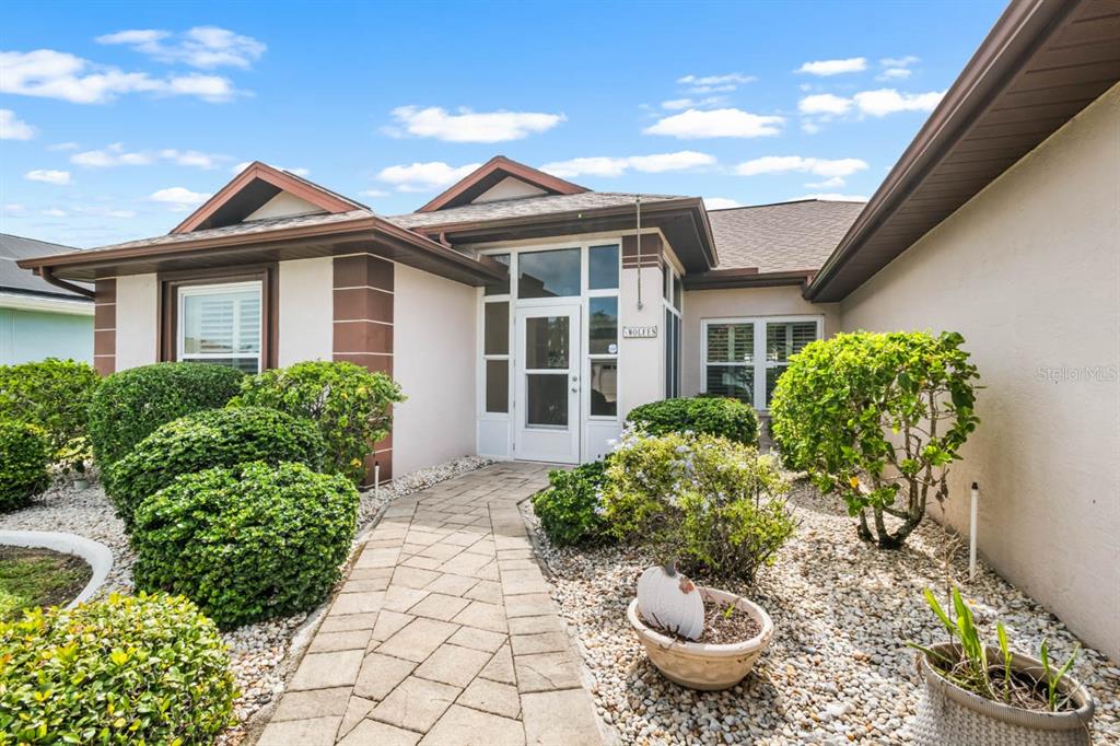A stone walkway leads to the front entrance of a house with beige stucco walls — 739 WINTERBROOKE WAY, SUN CITY CENTER, FL