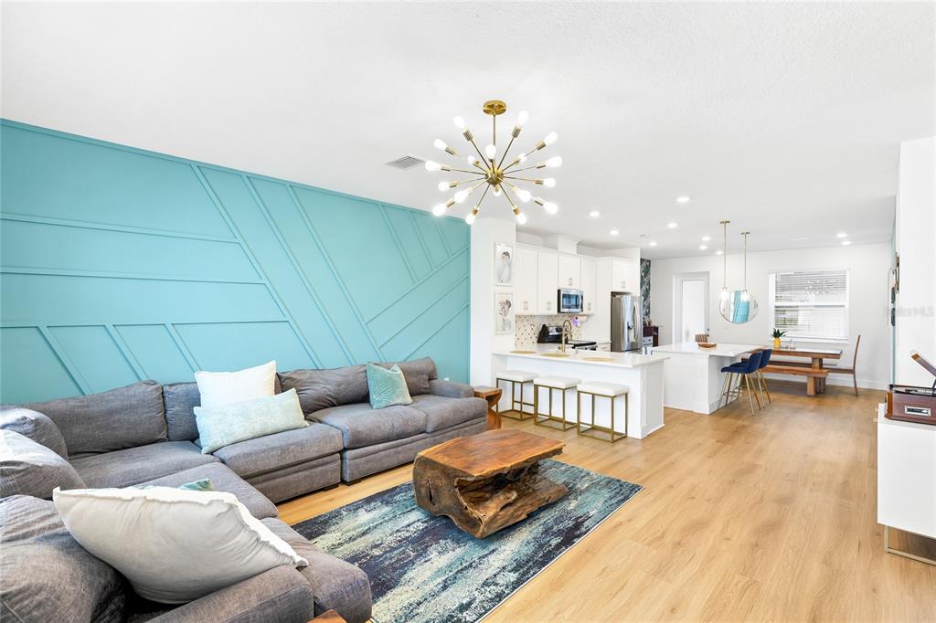 A living room features a teal accent wall, gray sectional sofa, and open-concept kitchen — 1808 FENDER LANE, SARASOTA, FL