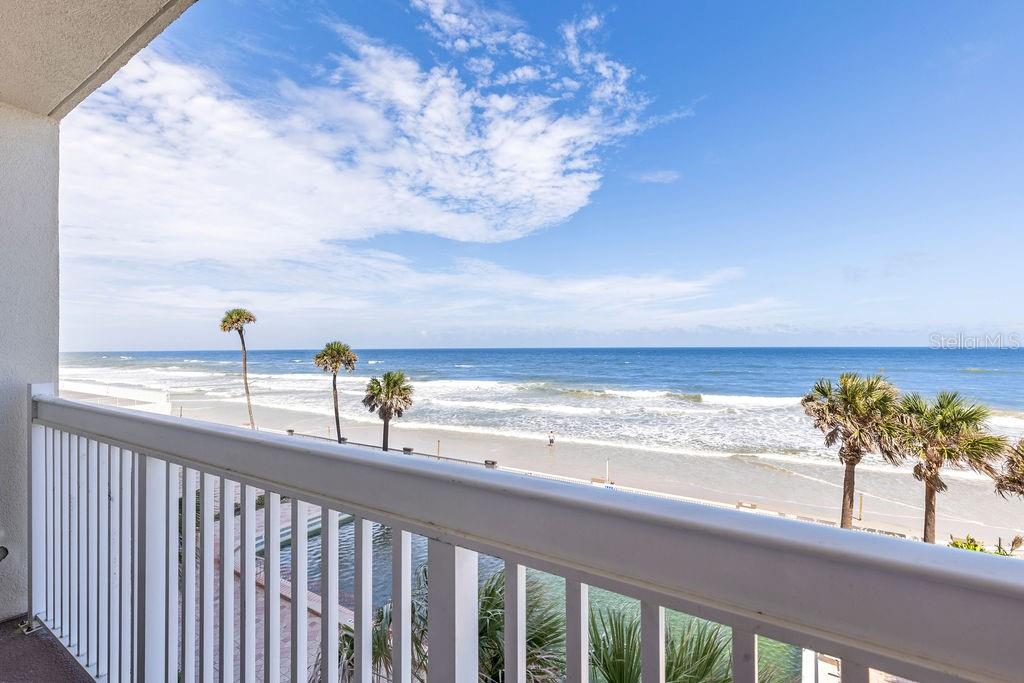 A balcony overlooks a sandy beach, ocean waves, and several palm trees under a blue sky — 2700 N ATLANTIC AVENUE UNIT 342, DAYTONA BEACH, FL