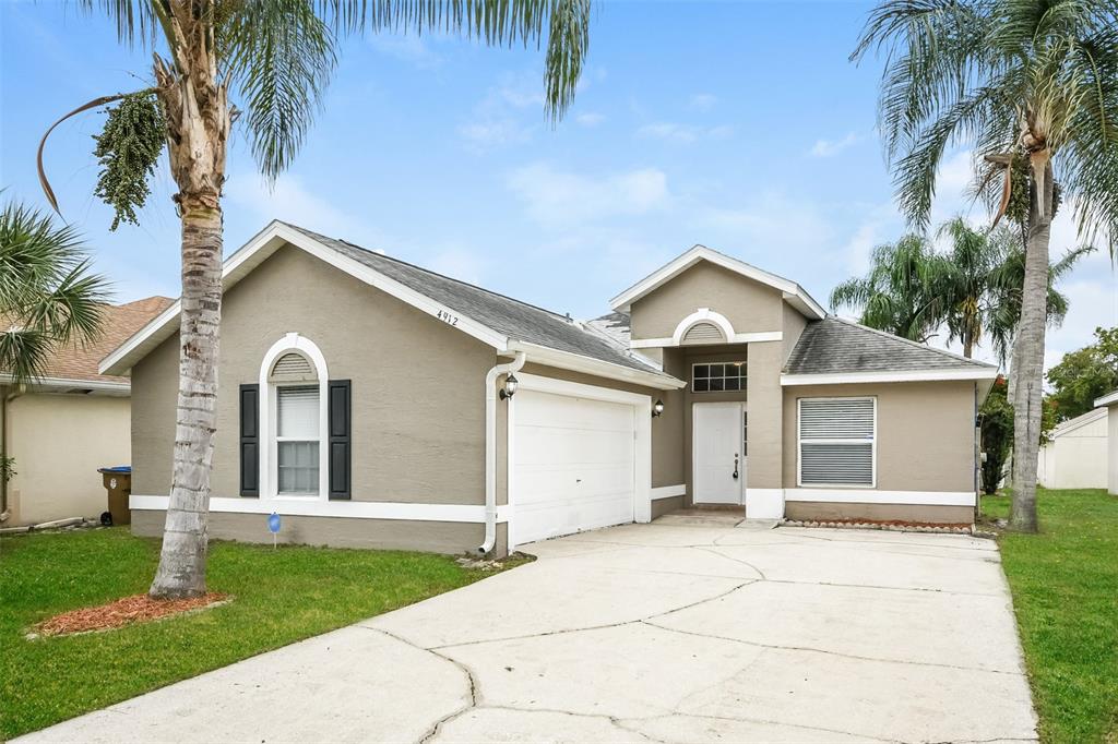 A single-story house with a beige stucco exterior, a two-car garage, and two palm trees — 4912 SAUSALITO LANE, KISSIMMEE, FL