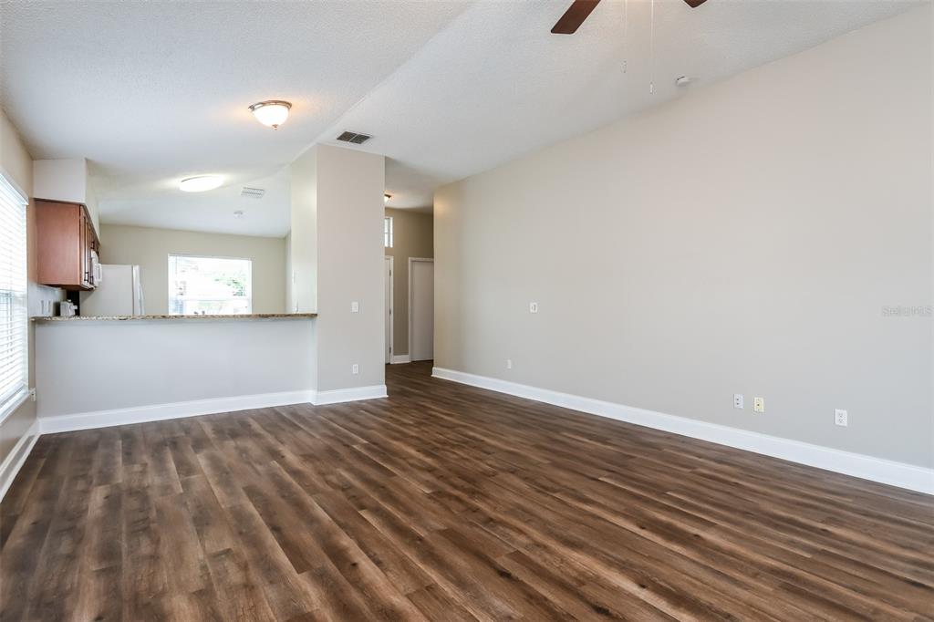 An open-concept living area features wood-look flooring, light-colored walls, and a kitchen breakfast bar — 4912 SAUSALITO LANE, KISSIMMEE, FL