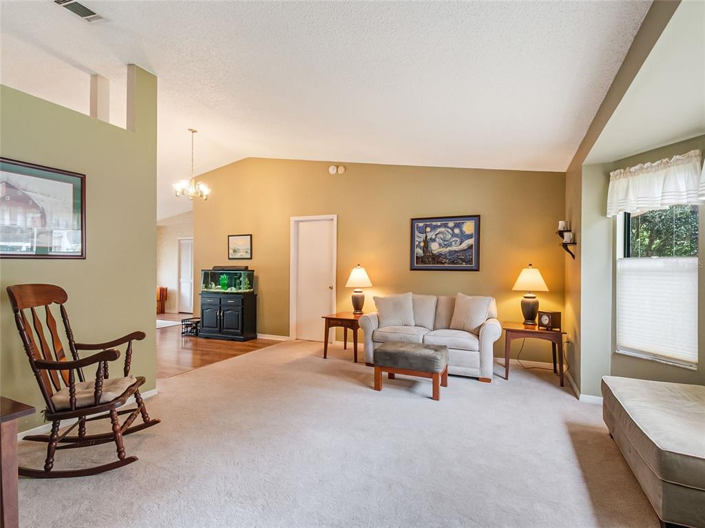 A living room features beige walls, carpeted flooring, a rocking chair, and a loveseat — 1321 WOOD LAKE CIRCLE, ST CLOUD, FL