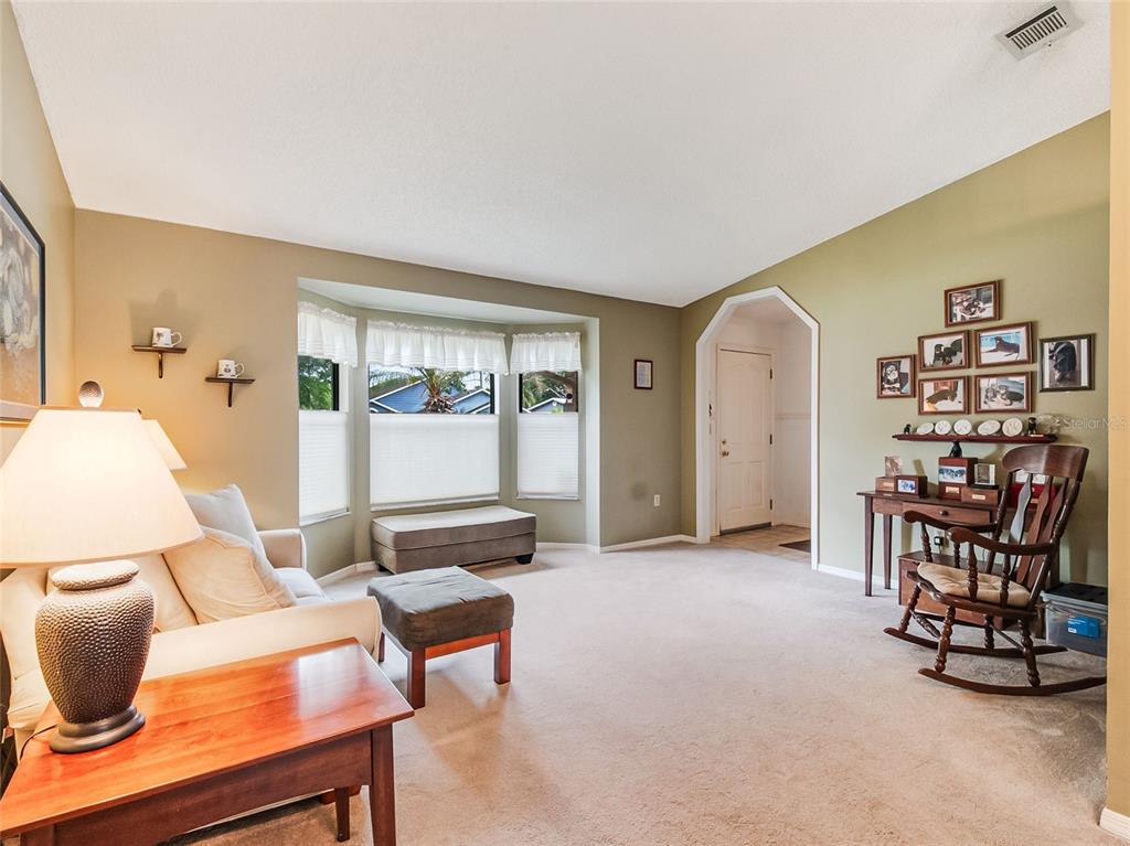 A living room with beige carpet, a bay window, and a wooden rocking chair — 1321 WOOD LAKE CIRCLE, ST CLOUD, FL