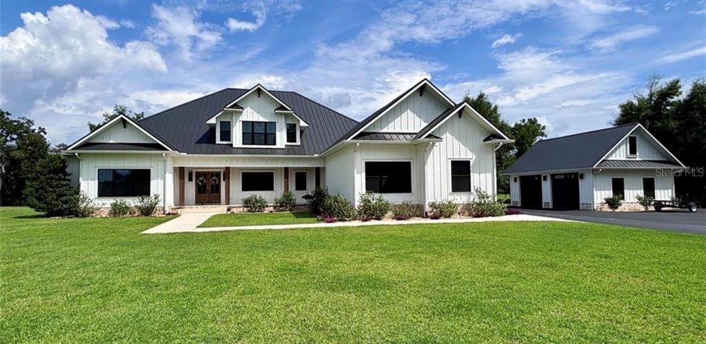 A white farmhouse with a black metal roof and a detached garage sits on grass — TBD HWY 329, REDDICK, FL