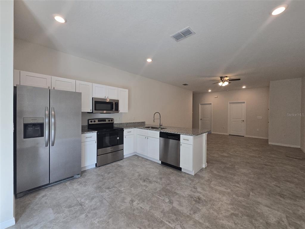 A kitchen features stainless steel appliances, white cabinetry, granite countertops, and light gray tile flooring — 546 IMPERIAL PL, KISSIMMEE, FL