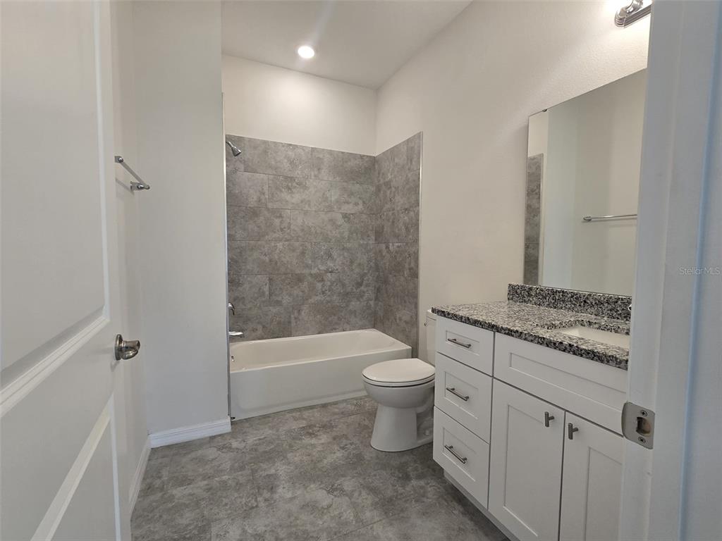 A bathroom features a white vanity with a granite countertop, toilet, and a tiled tub — 546 IMPERIAL PL, KISSIMMEE, FL